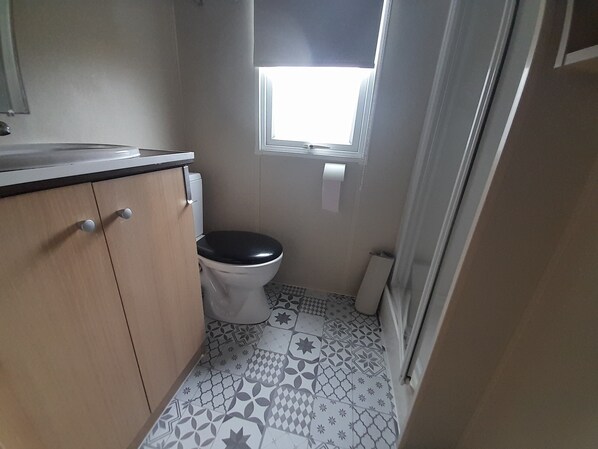 A small bathroom with a toilet, a sink, and a window. - Mobile Home Le Plein Soleil camping CLICOCHIC (Bernières-sur-Mer)