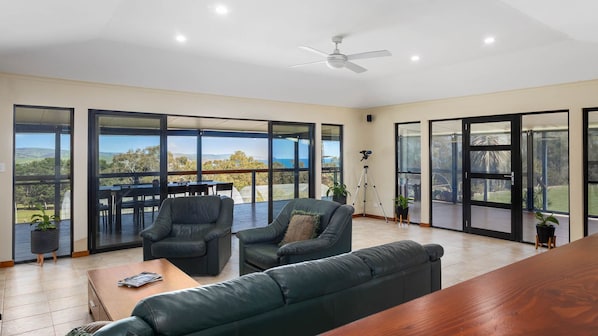 A spacious room with a large sliding glass door leading to an outdoor area, a ceiling fan, and a wooden coffee table. - Lot 4 Retreat - 150 Willson Drive (NORMANVILLE)