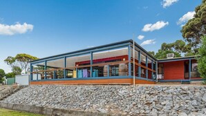 A modern house with a large glass facade, a wooden deck, and a stone retaining wall. - Lot 4 Retreat - 150 Willson Drive (NORMANVILLE)