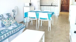 Un espace de vie compact comprenant un coin repas, une kitchenette et un canapé agrémenté d’un linge de lit à motifs.