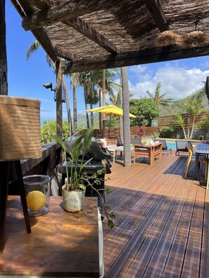 An outdoor wooden deck with a thatched roof, a table with a potted plant, and a yellow umbrella.
