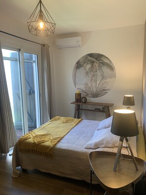 Un dormitorio con cama, una mesita de noche con lámpara, aire acondicionado de pared y una gran obra de arte circular en la pared.
