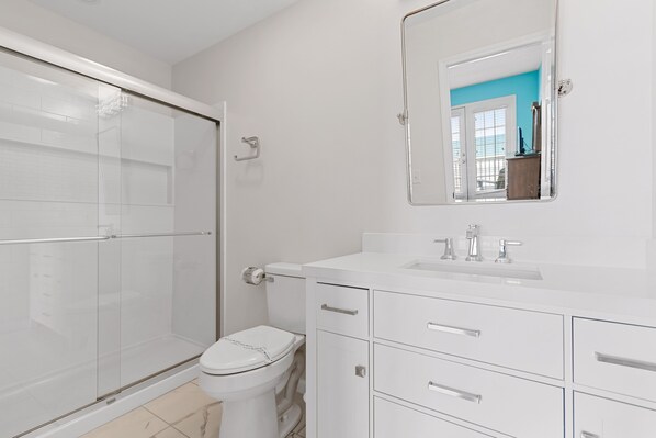 A modern bathroom with a glass shower enclosure, a toilet, and a vanity with drawers and a mirror.