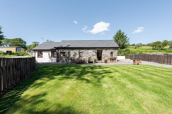 A stone house with a sloped roof, a fenced yard, and a wooden deck. - Eisteddfa - Glas y Dorlan - sleeps 4 guests  in 2 bedrooms (Criccieth)