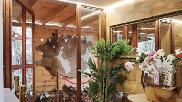 Ein Zimmer mit Holzboden, einem großen Spiegel, einer Topfpflanze und einer Vase mit Blumen.