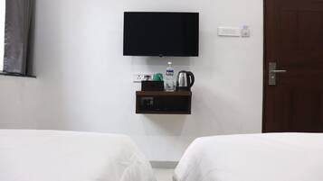 Habitación de hotel con dos camas, un televisor montado en la pared, un estante pequeño con una tetera, una botella de agua y un enchufe.