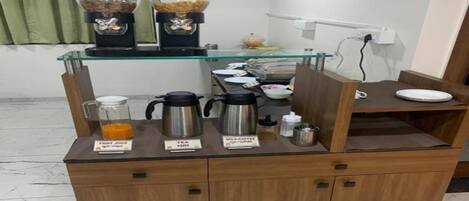 A coffee station with a glass top counter, coffee makers, and a milk dispenser.