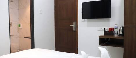 Una habitación de hotel con una cama, una puerta de madera, un televisor y una pequeña repisa con artículos de tocador.