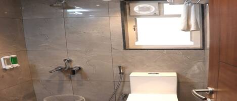A bathroom with a shower, toilet, and a window.
