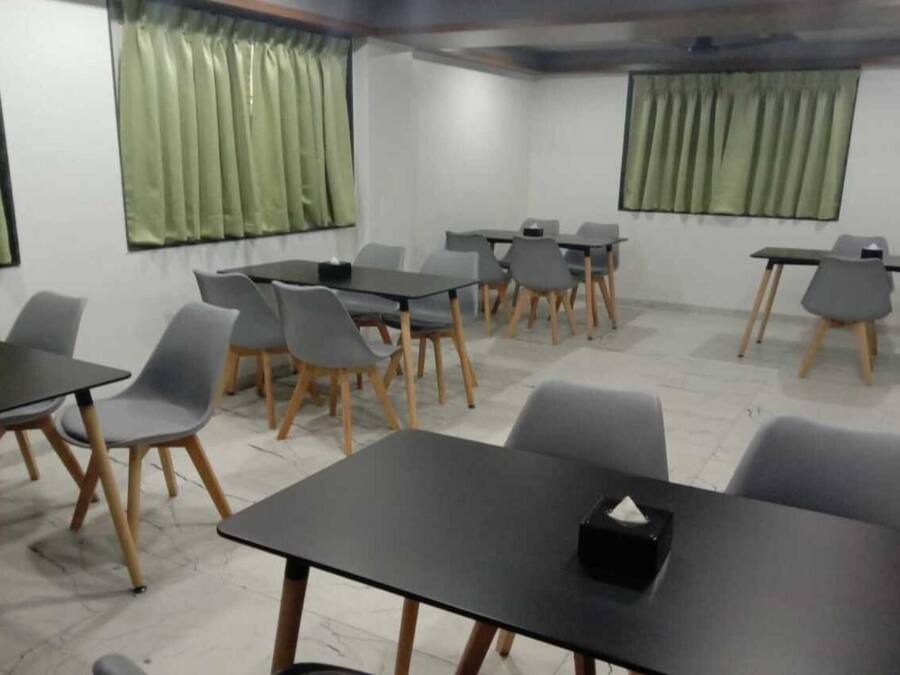 A conference room with multiple tables and chairs, green curtains, and a tiled floor.