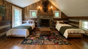 A log cabin bedroom with two beds, a fireplace, and a ceiling fan.