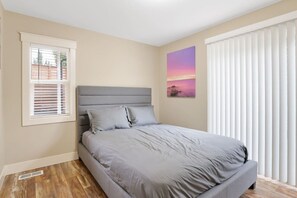 Une chambre à coucher avec un lit, une fenêtre avec des stores, un radiateur et un tableau accroché au mur.