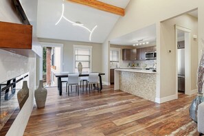 A modern kitchen with a central island, wooden flooring, and a dining area with a table and chairs. - Star Lake Waterfront “DUO” Homes (Federal Way)