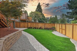 Un jardin avec une clôture en bois, un chemin en briques et une pelouse bien entretenue.