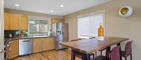 A modern kitchen with wooden cabinets, a stainless steel refrigerator, and a wooden dining table with red chairs.