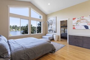 Um quarto com uma janela grande, uma cama, um banco e uma cômoda.