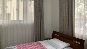 Ein Schlafzimmer mit einem Bett, einem Fenster mit durchsichtigen Vorhängen und Blick nach draußen.