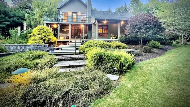 A two-story house with a balcony, a covered porch, and a well-maintained garden with a stone pathway leading to the entrance. - Hummingbird Hideaway (Galeton)