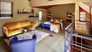 A spacious loft with a high ceiling, exposed wooden beams, a loft bed, a sofa, a coffee table, and a staircase. - Hummingbird Hideaway (Galeton)