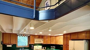 A modern kitchen with a central island, wooden cabinets, and a stainless steel refrigerator. - Hummingbird Hideaway (Galeton)