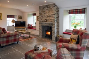 A cozy living room with a stone fireplace, plaid furniture, and a television. - Stunning coach house conversion (Perth)