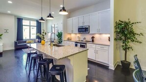 A modern kitchen with white cabinets, a granite countertop, and a central island with bar stools. - 5 Mins to Belmont and Vandy, Rooftop Deck, Garage  |  4 Bedroom Home with Rooftop and Grill, 10 Mins to Broadway, Perfect for Groups, 24 Hour Hospitality, Also Available for Long Term Rental (Nashville)