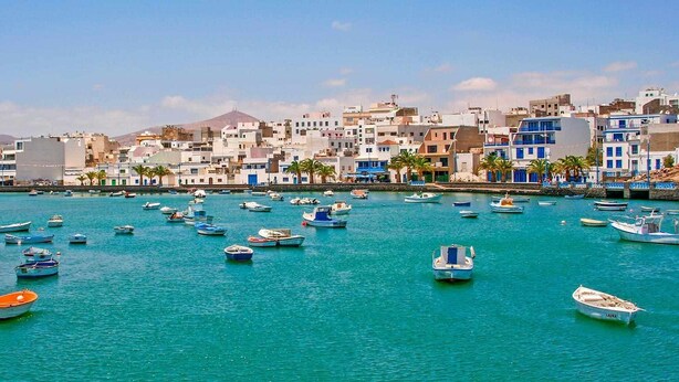 Un pueblo costero con numerosos barcos amarrados en un puerto deportivo, rodeado de edificios con balcones y palmeras.