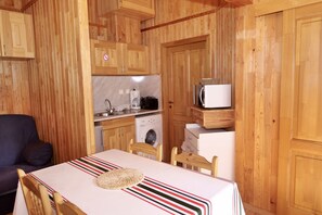 Compact kitchen area with microwave, coffee maker, and washing machine, adjacent to a dining area with a table for two.