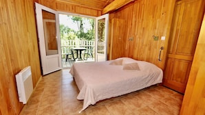 A wooden-paneled room with a bed, a radiator, and a sliding glass door leading to an outdoor area with a table and chairs.