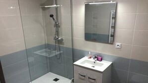 Une salle de bain moderne avec une douche à parois de verre, un lavabo blanc avec un miroir au-dessus et des toilettes.