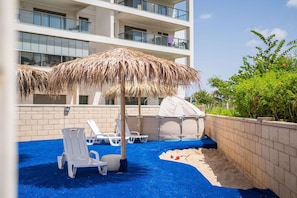 A rooftop pool area with lounge chairs, a thatched umbrella, and a covered seating area.