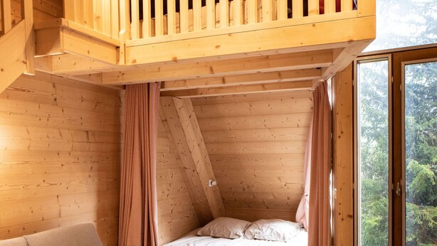A cozy cabin interior with a loft bedroom, a sofa, a chair, and a table with a mug.