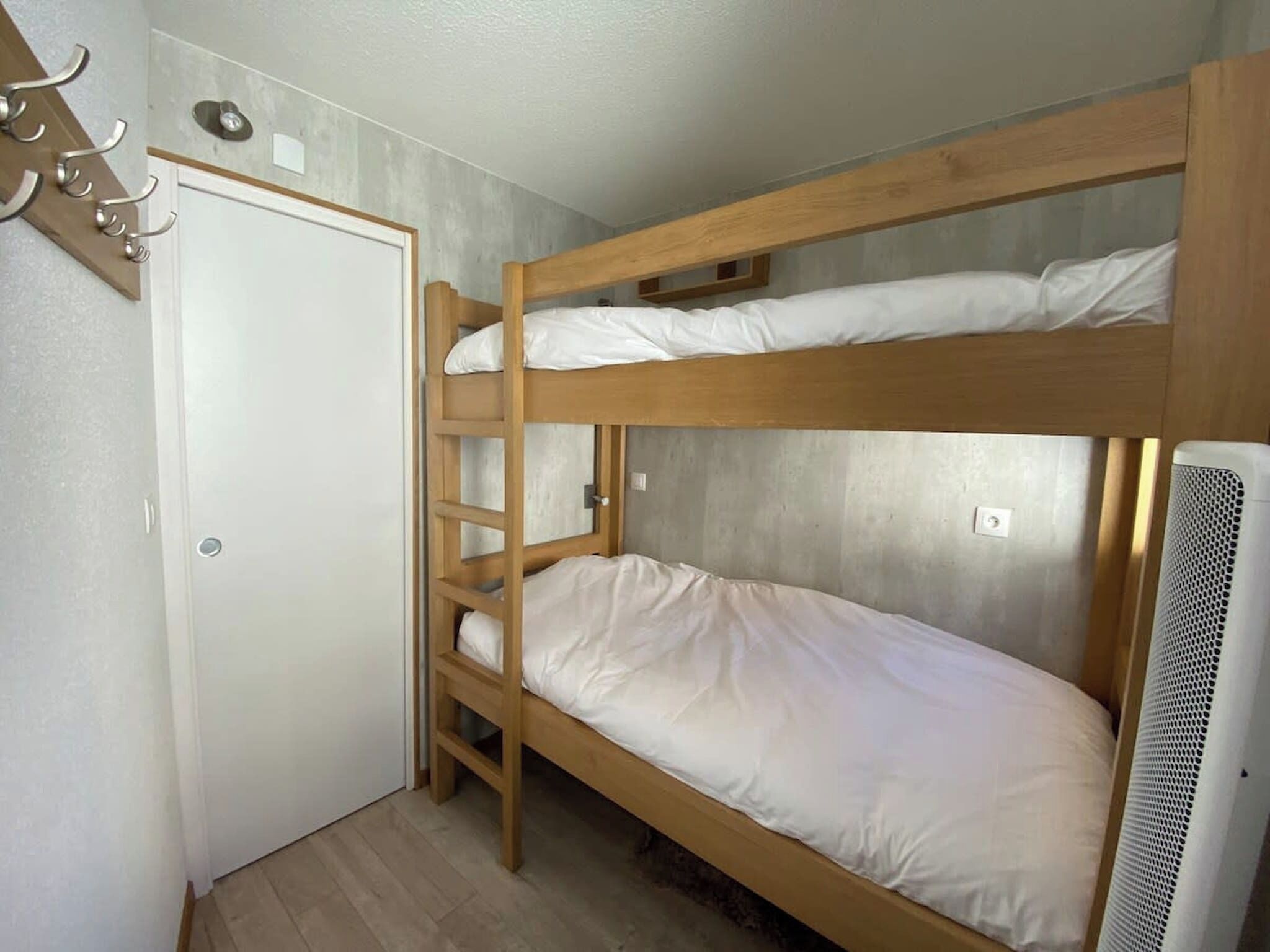 A bunk bed room with a wooden ladder, a white door, and a white radiator.
