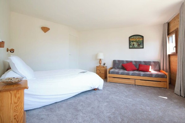 A bedroom with a bed, a bedside table, a nightstand, a sofa, and a wall-mounted picture.