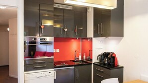 Eine kompakte Küche mit modernen Geräten, einer roten Akzentwand und einem Essbereich mit Holztisch und weißen Stühlen.