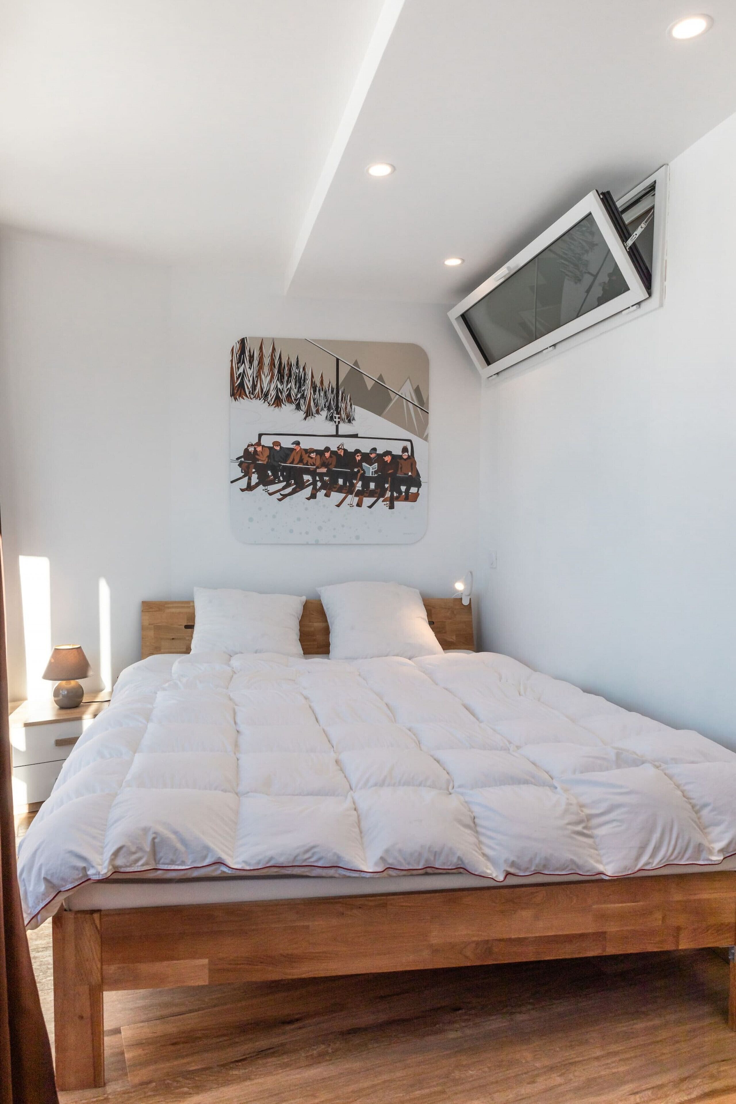 Une chambre à coucher avec un lit en bois, du linge de lit blanc, un téléviseur fixé au mur et un tableau au-dessus du lit.