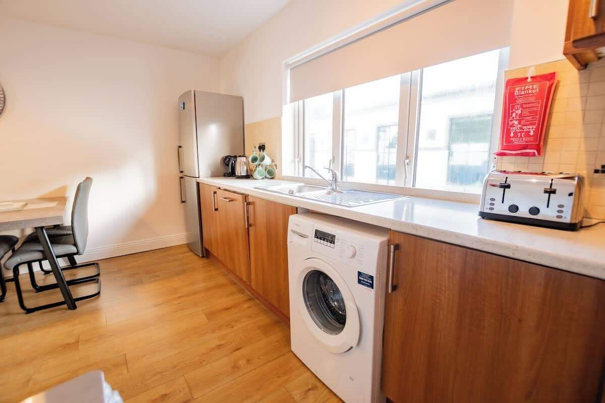 A compact kitchen with a washing machine, a toaster, and a window with a fire blanket hanging on the wall.