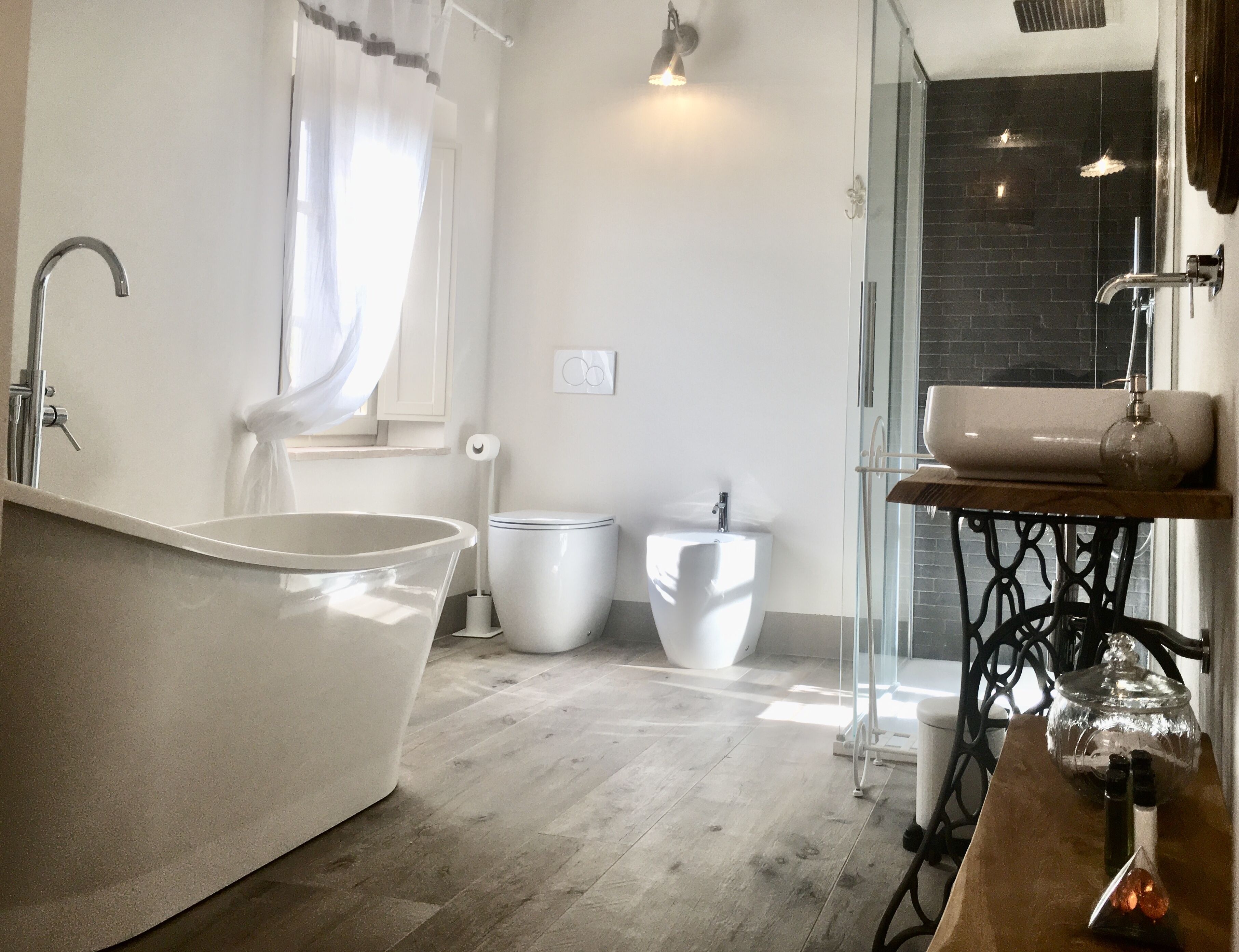Een moderne badkamer met een vrijstaand bad, een douche met glazen wanden en een houten wastafelmeubel met een glazen pot.