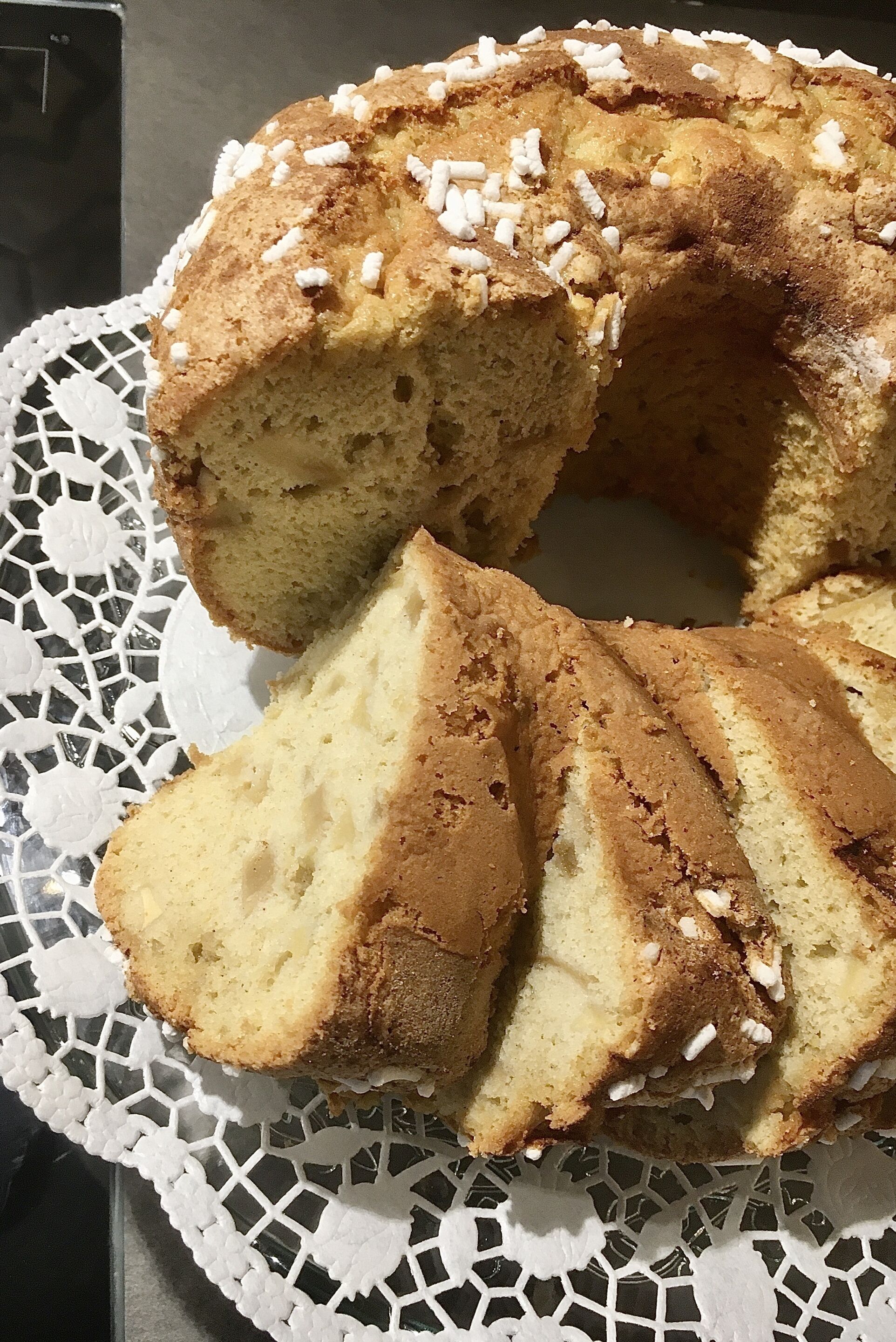 A bundt cake with white sprinkles on a lace doily.