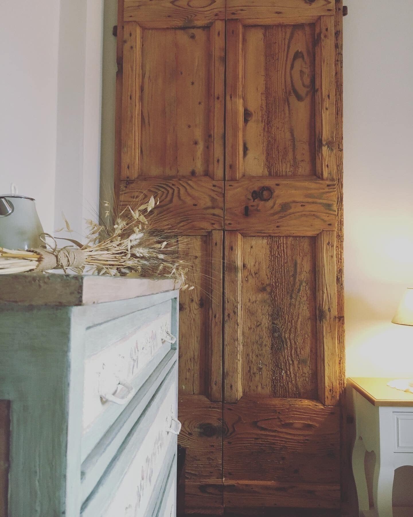 Un armadio in legno dal design rustico, una caraffa in metallo sopra e piante essiccate accanto.