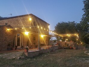 A stone building with a covered patio area adorned with string lights. - Vento Dorcia (Pienza)