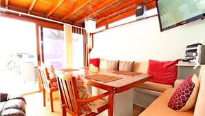 A cozy room with a wooden dining table, chairs, a sofa, and a television mounted on the wall. - Luxurious 2 Bed Villa (Montaña Roja, Playa Blanca)