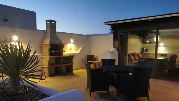 An outdoor patio area with a brick barbecue, wicker furniture, and a potted plant. - Luxurious 2 Bed Villa (Montaña Roja, Playa Blanca)