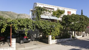 Un immeuble de deux étages avec une façade blanche, un balcon et une voiture garée devant.