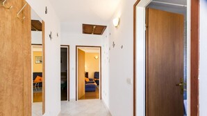 Un couloir avec une porte en bois sur la droite, un miroir sur la gauche et deux portes donnant sur des pièces dont le mobilier est bleu et orange.