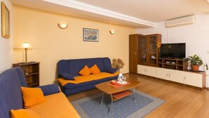 Un salon avec un canapé bleu, des coussins orange, une table basse en bois, un téléviseur et un meuble.