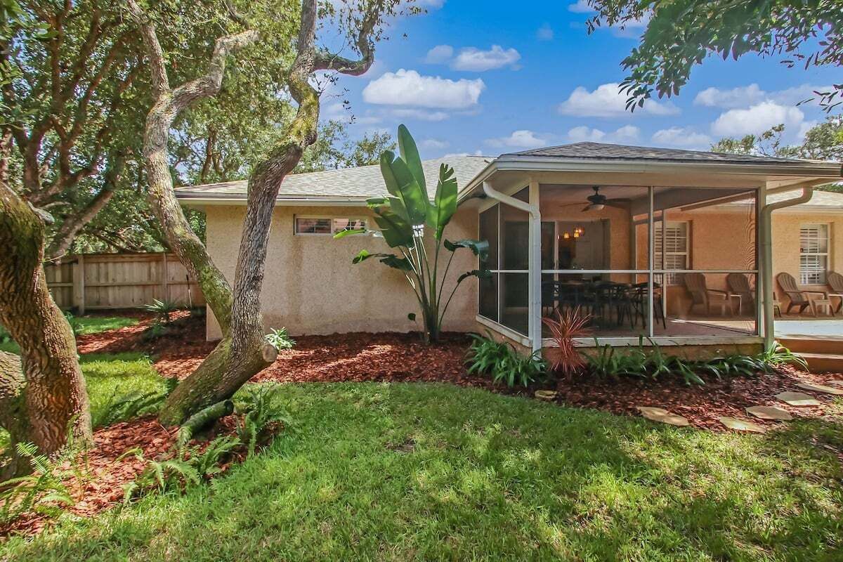 A house with a covered patio, a fenced yard, and a large tree.