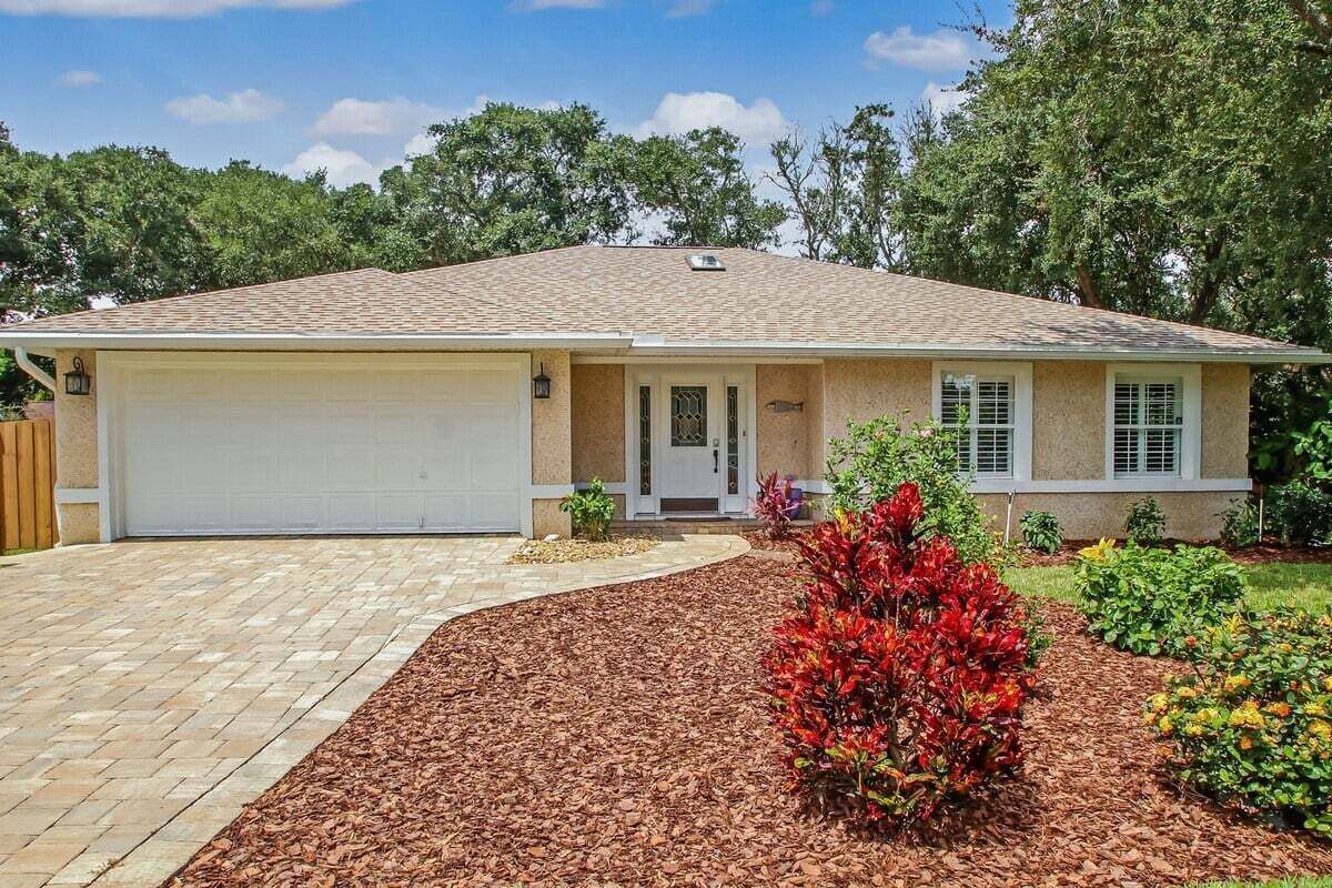 A single-story house with a garage, a front porch, and a landscaped garden with various shrubs and flowers.
