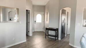 A hallway with a wooden floor, a dark wooden bench, and a white door with an arched window. - Centrally Located River Home with Mountain Views! (Fort Mohave)