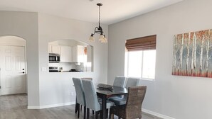 A dining area with a table and chairs, a kitchen in the background, and a window with blinds. - Centrally Located River Home with Mountain Views! (Fort Mohave)